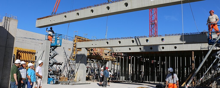 Bauherr und Baufirma schauen zu, wie die Betonträger montiert werden. bär