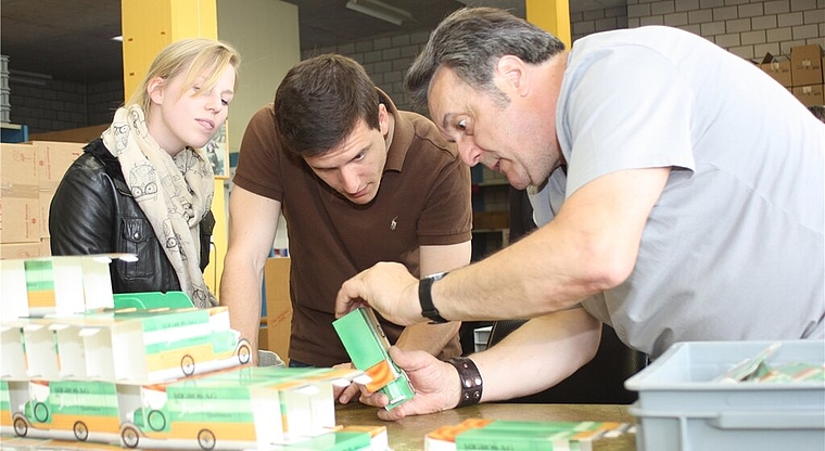 Felix Salzmann (r.) zeigt den Besuchern Mathias Welti und Nathalie Hofstetter in der Verpackungs-Werkstatt, wie man faltet.Foto: zVg