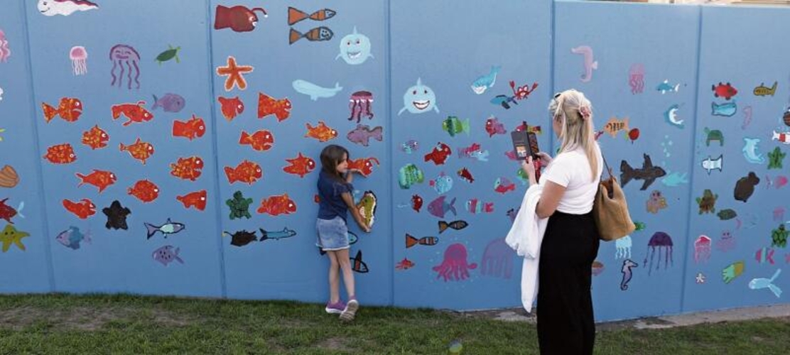 Die Zweitklässlerin Amelia posiert für ihre Mutter Leonida Halili vor der Wand mit dem Seepferdchen, das sie gemalt hat. bär