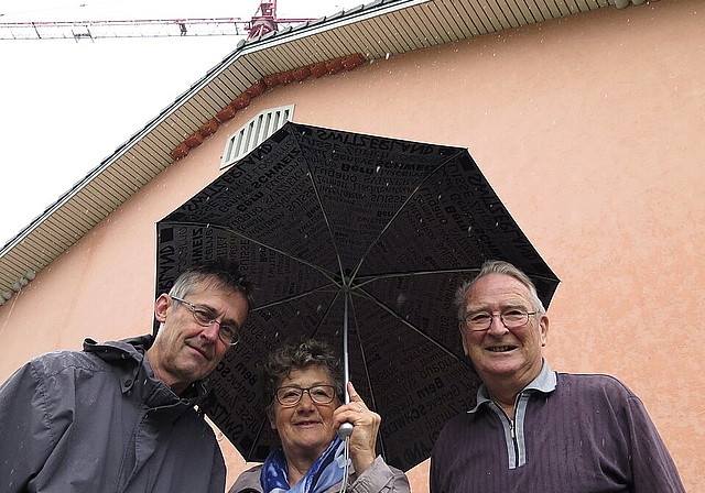 Vogelschützer Andres Beck, Susanne Hobbs, Fernand Herrmann (v.l.). Unter dem Vordach der Turnhalle haben sie Kunstnester für Mehlschwalben (links und rechts, grau) und Mauersegler (im Giebel, rötlich) montiert.Foto: Mü
