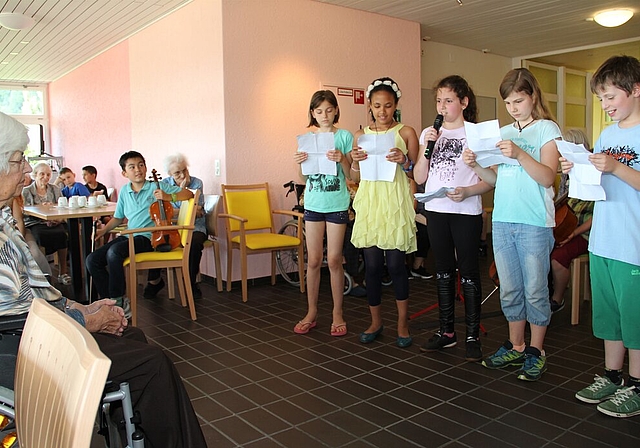 Die Kinder tragen Geschichten und Gedichte vor. Warm-up mit Ballonen. Lilo Jud, Fachstelle Altersfragen und Freiwilligenarbeit in Wettingen (Mitte) im Gespräch mit einer Seniorin und zwei Schülerinnen. Gemütliches Beisammensein bei Kaffee und Berl