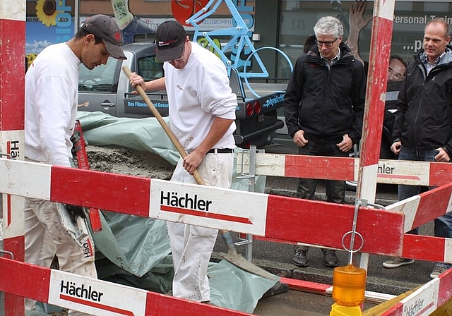 Handwerker bauen Poller ein für die neuen Tempo-30-Zonen, Urs Heimgartner (r.), Leiter Bau und Planung, und Gemeinderat Markus Maibach schauen zu. Foto: bär