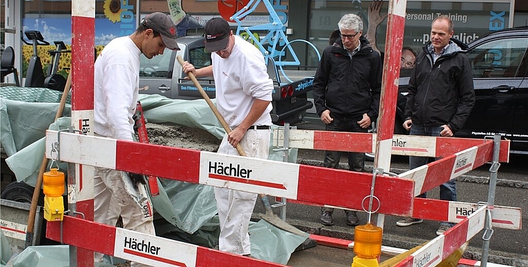 Handwerker bauen Poller ein für die neuen Tempo-30-Zonen, Urs Heimgartner (r.), Leiter Bau und Planung, und Gemeinderat Markus Maibach schauen zu. Foto: bär