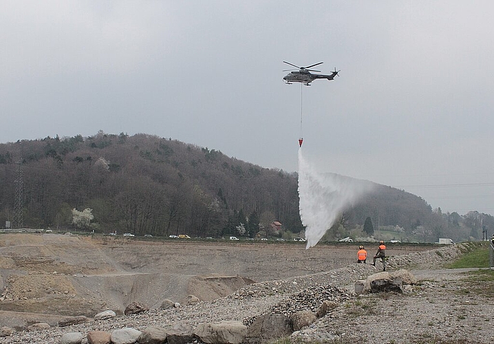 Der Helikopter, <em>ein Super Puma, wirft Wasser aus der Limmat über der Kiesgrube in Wettingen ab.</em><em>Rahel Bühler</em>
