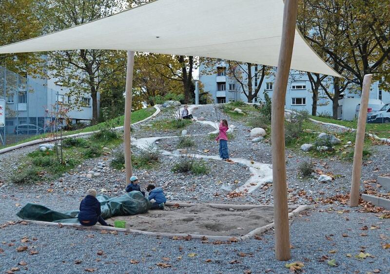 Hügel mit Wasserspiel, der Sandkasten ist unter dem Sonnensegel platziert. ihk
