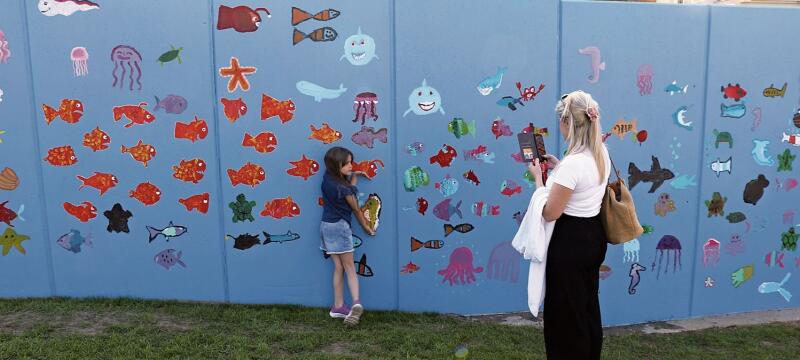 Die Zweitklässlerin Amelia posiert für ihre Mutter Leonida Halili vor der Wand mit dem Seepferdchen, das sie gemalt hat. bär