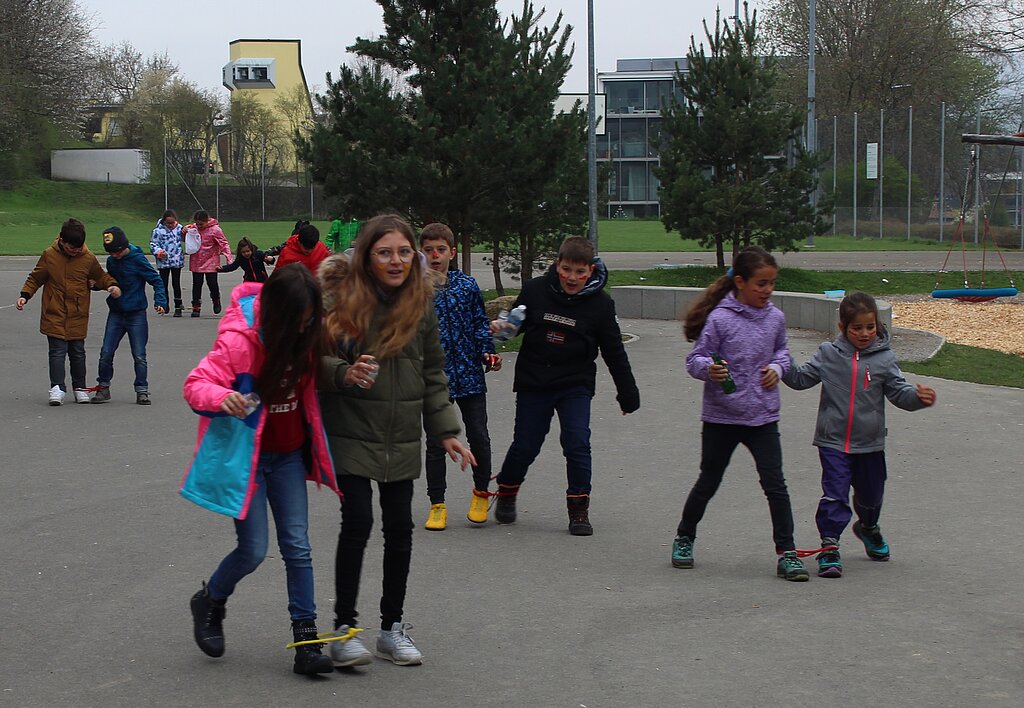 Spielerisch Abfall <em>suchen: Mit zusammengebundenen Beinen bringen die Schüler den gefundenen Müll zur Sammelstelle.</em>